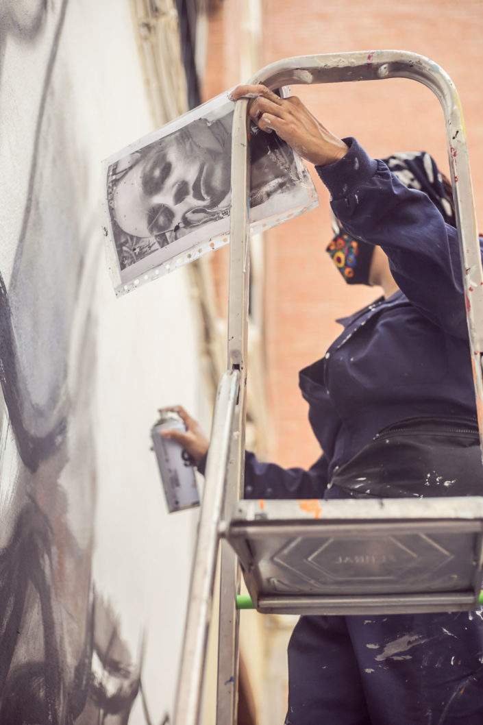 Mujer artista encima de una escalera pintando un mural con spray