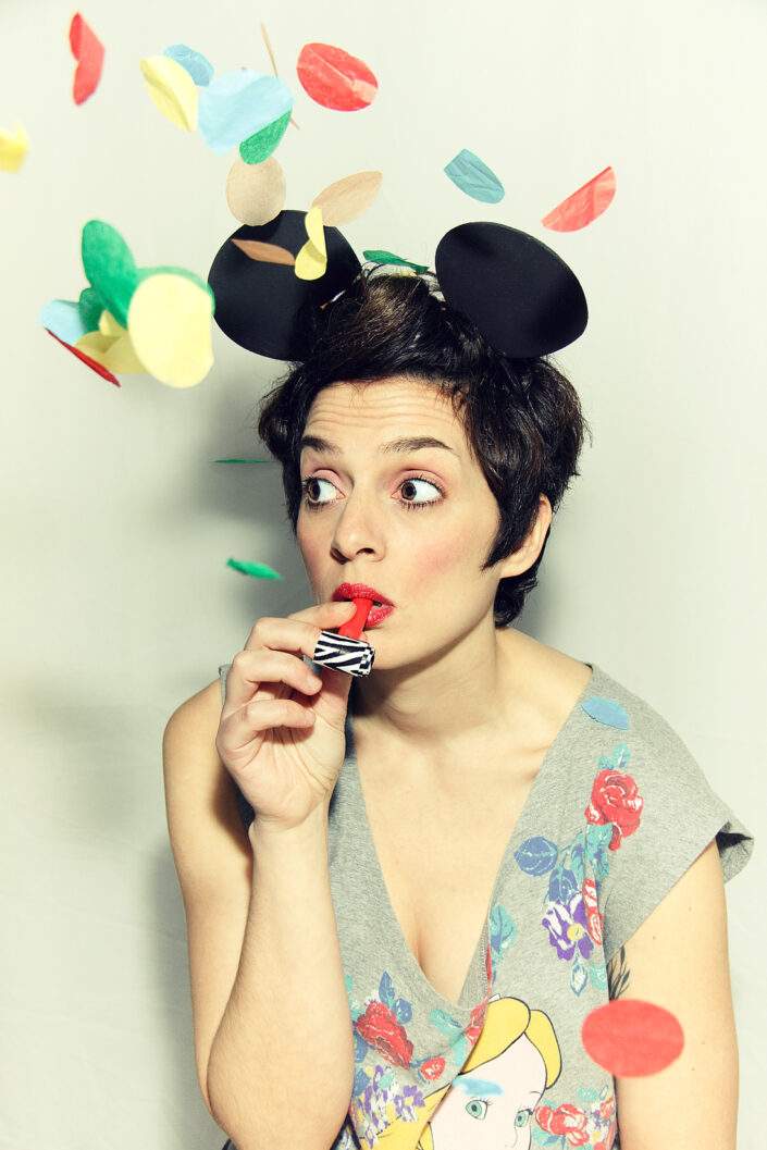 Retrato colorido de mujer con orejas de disfraz de Mickey Mouse, espantasuegras y confetis.
